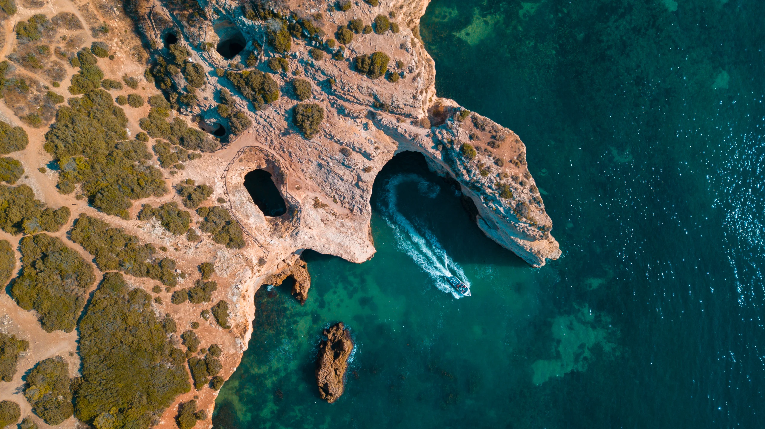 aerial-view-turquoise-shiny-sea-with-single-boat-sailing-along-coastal-cliff-algarve